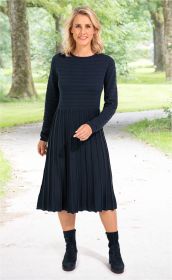 Frau trägt navyblaues, langärmliges Baumwoll-Kleid mit feinen Quer- und Längsrippen, knieumspielendem Rock, stehend auf Gehweg mit grünen Bäumen im Hintergrund, kombiniert mit schwarzen Stiefeletten