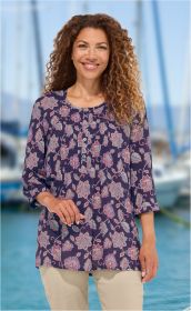 Frau mit lockigen Haaren trägt marineblaue Modal-Bluse mit floralem Muster und Knopfleiste, steht vor verschwommenem Hafen mit Wasser und Segelbooten, beige Hose