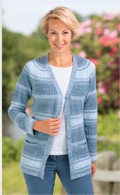 Frau trägt blaue Baumwoll-Strickjacke mit Knöpfen, zwei Taschen, kombiniert mit weißem Shirt und blauen Jeans, steht vor unscharfem, grünen Hintergrund mit rosa Blüten