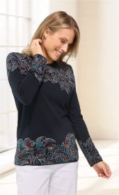 Frau trägt schwarzen Baumwoll-Pullover mit buntem abstraktem Muster an Oberteil, Ärmel und Saum, steht seitlich, lächelt und hält Hand an Haar, kombiniert mit weißer Hose, heller Hintergrund