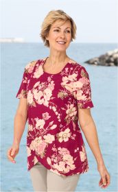 Frau am Meer trägt rote Baumwoll-Mix-Bluse mit beigem Blumenmuster, kurzen Ärmeln und asymmetrischem Saum, beige Hose, lächelt und schaut nach rechts