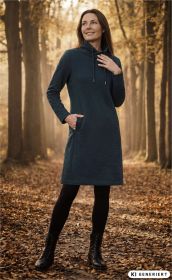 Frau trägt grünes Baumwoll-Kleid mit hohem Kragen und Taschen, schwarze Leggings und Stiefel, steht lächelnd auf mit Herbstlaub bedecktem Waldweg, Sonne scheint durch Bäume, herbstliche Atmosphäre