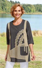 Frau mit blonden, kurzen Haaren trägt dunkelgraue Baumwoll-Mix-Tunika mit hellbeigen Einsätzen, floralen Häkelmustern und Brusttasche, steht vor See mit Wald im Hintergrund, lächelt, trägt weiße Hose