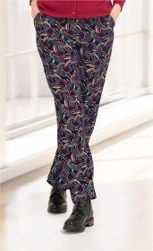 Beinansicht einer Viskose-Hose mit buntem, kreisförmigem Muster in Dunkelblau, Rot und Beige, kombiniert mit schwarzen Schnürstiefeln und rotem Oberteil, Hände in den Taschen, stehend auf hellem Boden in hellem Innenraum