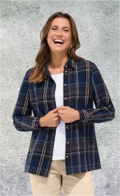 Frau trägt lächelnd eine baumwoll-Bluse mit blauem, braunem und weißem Karomuster, beige Hose und weißes Shirt, steht vor grauer Wand