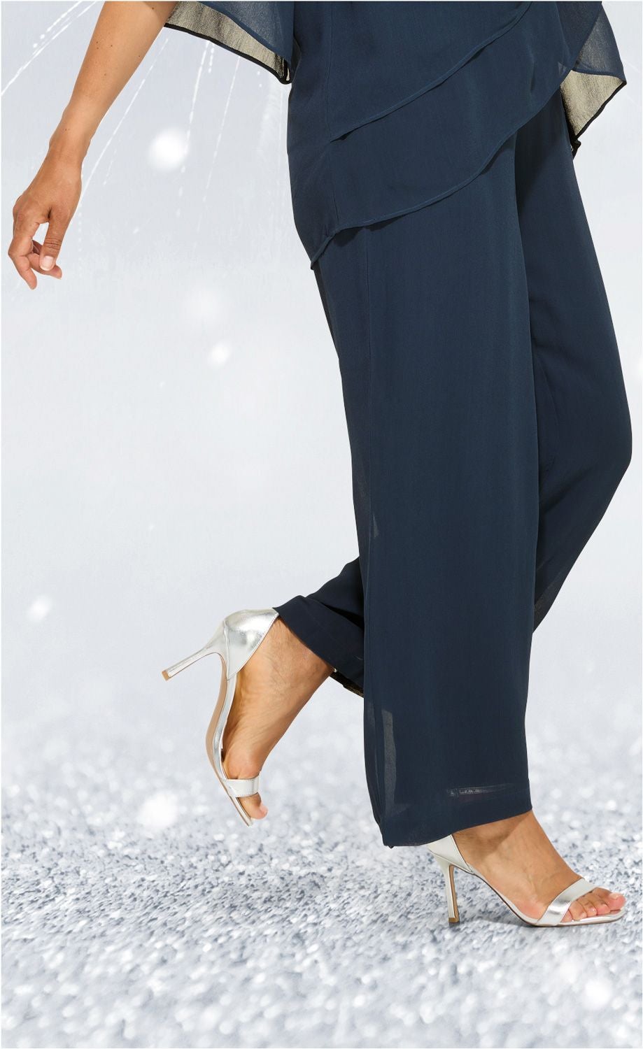 Dunkelblaue Viskose-Hose in weiter Passform, kombiniert mit silberfarbenen High-Heel-Sandalen, weiches fließendes Material, angeschnittener Saum, sitzend bis zum Knöchel, Teil eines festlichen Outfits.