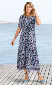 Frau am Meer auf Holzsteg trägt blaues Viskose-Maxikleid mit floralem Muster in Blau und Orange, halblange Ärmel, Raffung in der Taille, Kleid endet knapp oberhalb der Knöchel, kombiniert mit blauen Espadrilles mit Schnürung