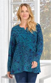 Frau trägt langärmlige Viskose-Bluse in Blau mit türkisfarbenem, floralem und ornamentalem Muster, kleiner V-Ausschnitt, kombiniert mit blauer Jeans, stehend vor Fenster mit Sonnenschein und grünen Pflanzen draußen