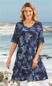 Frau am Strand trägt blaues Baumwoll-Mix-Kleid mit V-Ausschnitt und hellblauem Blumenmuster, kurze Ärmel, leichte Doppel-Lagen-Optik, kombiniert mit weißen Leggings, blonder welliger mittellanger Haarstil, lächelnd