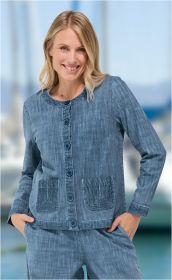 Frau trägt blaue Baumwoll-Jacke mit Rundhalsausschnitt, Knopfleiste und aufgesetzten Taschen, lächelnd vor verschwommenem maritimem Hintergrund, Hände in Taschen der passenden Hose.