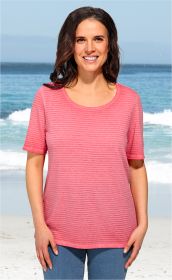 Frau am Strand trägt pink gestreiftes Baumwoll-Mix-Shirt mit kurzen Ärmeln und Rundhalsausschnitt, dazu blaue Jeans, lächelt freundlich, Meer und Wellen im Hintergrund sichtbar.