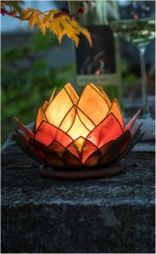 Capiz Windlicht in Form einer Lotusblüte mit warm leuchtenden, goldgelben und roten Perlmuttblättern, beleuchtet auf einer Steinoberfläche im Freien bei Dämmerung, mit unscharfem Hintergrund und herbstlich gelbem Blattzweig darüber