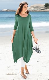 Frau am Strand trägt grünes, locker fallendes Viskose-Kleid mit asymmetrischem Saum und 3/4-Ärmeln, hält schwarze Sandalen in der Hand, barfuß im Sand, blauer Himmel und Meer im Hintergrund