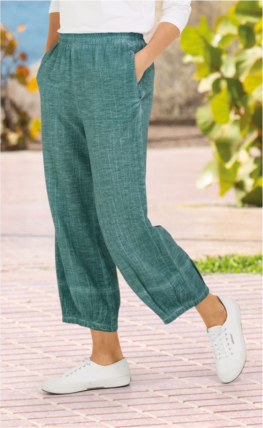 Baumwoll-Hose in Türkis mit elastischem Bund, bequemer weiter Schnitt, seitliche Eingrifftaschen, getragen mit weißen Sneakern auf gepflastertem Weg vor sommerlicher Außenkulisse mit grünen Pflanzen.