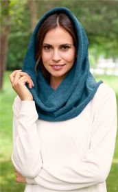Frau trägt blauen Alpaka-Schal als Kapuze, cremefarbener Pullover, stehend im grünen Park, lächelt leicht, Nahaufnahme