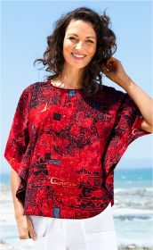 Lächende Frau am Meer trägt rotes, kurzärmeliges Baumwoll-Shirt mit abstraktem schwarzen und blauen Muster, kombiniert mit weißen Hosen, hellblauer Himmel im Hintergrund