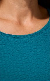 Ausschnitt eines Baumwoll-Mix-Shirts in Petrol mit feinem Strukturmuster, rundem Halsausschnitt, getragen von einer Person mit sichtbarem Hals und Schlüsselbeinbereich