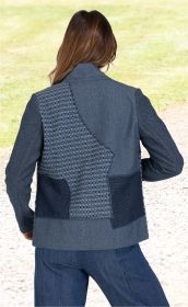 Rückansicht einer Frau mit langen braunen Haaren, die eine blaue Baumwoll-Mix-Jacke mit verschiedenen Struktur- und Musterflächen trägt, kombiniert mit blauer Jeans, stehend auf einem Weg bei grünem Gras im Hintergrund