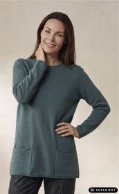 Frau mit braunen Haaren trägt grünen Merino-Mix-Pullover mit Rundhals, langen Ärmeln und zwei aufgesetzten Taschen, lächelt, steht vor hellem Hintergrund, rechte Hand an Hüfte, linke Hand am Hals.