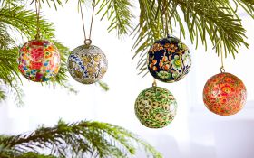 Fünf bunt handbemalte Hänger Kugeln mit floralem Muster, hängend an grünen Tannenzweigen vor hellem Hintergrund, Weihnachtsdekoration Set.