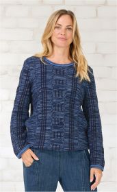 Frau trägt dunkelblauen Baumwoll-Pullover mit gemustertem Strickdesign, langärmlig, rundem Ausschnitt, kombiniert mit blauer Jeans, vor heller Backsteinwand, Hände in den Hosentaschen, lächelnder Gesichtsausdruck
