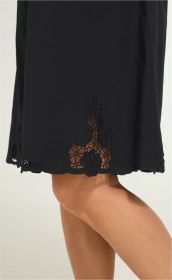 Schwarzes Baumwoll-Mix-Kleid mit floraler Spitzenstickerei am Saum, knielang, sichtbare Haut durch transparente Einsätze, Modell mit leicht gebeugtem rechten Bein vor hellem Hintergrund