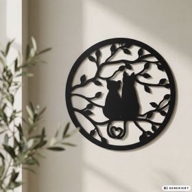 runde schwarze Wand-Deko aus Metall mit zwei sitzenden Katzen, die Schweife in Herzform formen, umgeben von Baumzweigen mit Blättern, moderne minimalistische Dekoration an cremefarbener Wand