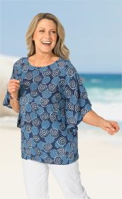 Frau in Viskose-Bluse mit blauem Spiralmuster, halblangen Ärmeln, steht lächelnd am Strand vor blauem Himmel und Meer, trägt weiße Hose und Armband, rechter Arm ausgestreckt