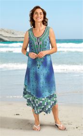 Frau am Strand trägt ärmelloses Viskose-Kleid in Blau mit grünen und weißen ethnischen Mustern, Knielang, sommerlich, mit Sandalen und Armband, lächelnd vor Meer und klarem Himmel.