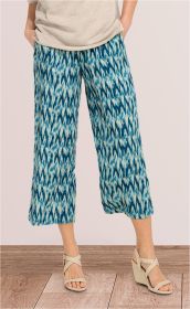 Damen Viskose-Hose mit blau-weiß gemustertem Ikat-Design, weiter Schnitt, knöchellang, kombiniert mit beigefarbenem Oberteil und hellen, gekreuzten Riemchen-Sandaletten mit Keilabsatz auf Holzfußboden