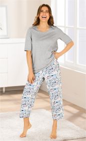 Frau in grauem Baumwoll-T-Shirt und gemusterter Baumwoll-Pyjama-Hose mit Paisley-Motiv, barfuß stehend auf weißem Teppich in hellem Raum mit Fenster, lacht und hält eine Hand in der Hosentasche