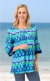 Frau am Strand trägt bunte Modal-Bluse in Blau- und Grüntönen mit 3/4-Ärmeln und Knopfleiste, blaue Jeans, lächelt, hellblonde lange Haare, Meereskulisse im Hintergrund