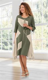 Frau trägt knielanges olivgrünes Baumwoll-Mix-Kleid mit asymmetrischen beigen Netz-Einsätzen, 3/4-Ärmeln, Rundhalsausschnitt und Kordelzug, kombiniert mit beigen Sandaletten, stehend vor großen Fenstern mit Blick ins Grüne