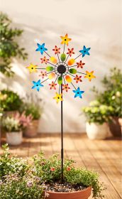 Bunter Deko-Gartenstecker mit rot-gelben, blauen und grünen Blumenmotiven auf schwarzem Stab, steckend in einem Blumentopf mit kleinen blühenden Pflanzen auf Holzterrasse, unscharfer Gartenhintergrund