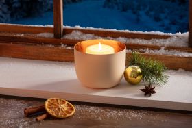 cremefarbener Teelichthalter mit brennendem Teelicht auf Fensterbrett, dekoriert mit Tannenzweig, goldenem Christbaumschmuck, Sternanis, getrockneter Orangenscheibe, Zimtstangen und Schneeflocken, winterliche Stimmung