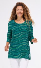 Frau mit langen Locken trägt grün-blaue Viskose-Bluse mit wellenförmigem Muster, 3/4-Ärmeln und seitlichem Schlitz, kombiniert mit weißen Hosen, vor hellem Hintergrund, lächelnd und in Bewegung.