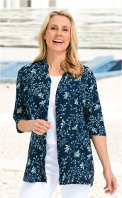 Frau trägt dunkelblaue Viskose-Bluse mit floralem Muster, 3/4-Ärmeln, offen über weißem Shirt, weiße Hose, lächelnd, helle Haare, stehender Hintergrund mit verschwommenem Außenbereich