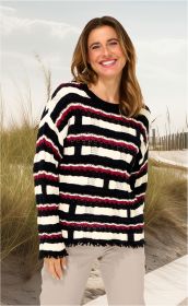 Frau trägt Baumwoll-Pullover mit breiten, bunten Streifen in Schwarz, Weiß und Bordeaux, stehend vor Strandlandschaft mit Dünen und Holzzaun, lächelnd, helle Hose, lange braune Haare, lockerer Schnitt