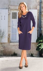 Frau mit langen blonden Haaren trägt ein elegantes dunkelblaues Baumwoll-Kleid mit 3/4-Ärmeln, seitlichen Taschen und Rundhalsausschnitt, kombiniert mit braunen Pumps und Perlenkette vor hellem Gebäude mit weißen Fensterläden