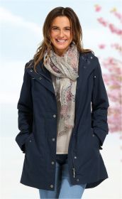Frau trägt dunkelblaue Baumwoll-Jacke mit Reißverschluss und Druckknöpfen, dazu gemusterten Schal in Pastellfarben, helles Shirt und blaue Jeans, lächelt vor hellem, unscharfem Hintergrund mit rosa Blüten.