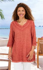Frau am Strand mit rot-orangefarbener Baumwoll-Bluse mit 3/4-Ärmeln und Spitzenbesatz am V-Ausschnitt, weißer Hose, brauner lockiger Haarpracht, lächelnd, Hintergrund mit Meer, Palmen und Holzstühlen