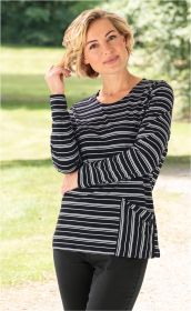 Frau im schwarzen Baumwoll-Shirt mit weißen horizontalen Streifen, lockige blonde Haare, steht draußen auf einem Weg mit grüner Wiese und Bäumen im Hintergrund, blickt freundlich in die Kamera