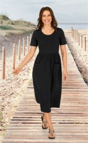 Frau in schwarzem Baumwoll-Kleid mit kurzen Ärmeln und Taschen, geht lächelnd barfuß mit Sandalen auf Holzsteg am Strand mit Meer und Dünen im Hintergrund