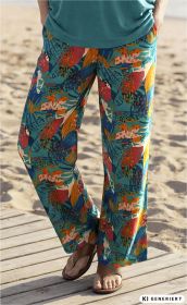 Beine einer Person am Strand mit bunter, locker sitzender Viskose-Hose in Türkis mit floralen und tropischen Mustern in Orange, Rot, Gelb und Weiß, dazu braune Flip-Flops auf Holzplanken.