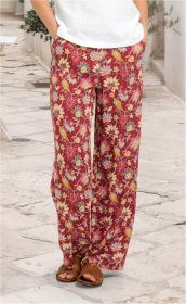 Frau trägt rote Viskose-Hose mit buntem Blumenmuster, weiße Bluse, braune Sandalen, steht auf gepflastertem Weg mit Pflanzkübeln im Hintergrund