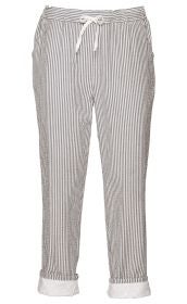 Baumwoll-Hose in Weiß mit engen grauen Streifen, elastischem Bund mit weißer Kordel zum Binden, seitlichen Eingrifftaschen und aufgekrempelten Beinenden mit weißem, besticktem Stofffutter.
