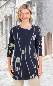 Frau mit kurzen blonden Haaren trägt dunkelblaues Baumwoll-Mix-Shirt mit langen Ärmeln und beige-grauen, wellenförmigen Linien und Spiralmustern, kombiniert mit hellen Hosen, vor steiniger Hausfassade auf gepflastertem Weg.