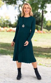 Frau in dunkelgrünem, langärmligem, geripptem Midi-Kleid mit schwarzen Stiefeln und rundem Spiralschmuck auf einem Gehweg im Park, lachend, im Hintergrund Bäume und Blumen, sonniger Tag