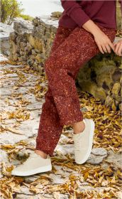 Person sitzt auf Natursteintreppe mit herbstlichen Blättern, trägt rot-braune gemusterte Viskose-Hose, beigen Sneaker und bordeauxfarbenen Pullover, Hände liegen entspannt auf den Knien