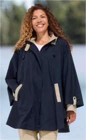 Frau mit lockigem Haar trägt eine dunkelblaue Baumwoll-Jacke mit hellbeigen Akzenten an Taschen, Ärmeln und Innenkragen, lächelt, Hände in Taschen, beiger Pullover und Hose, unscharfer Außenhintergrund mit Bäumen